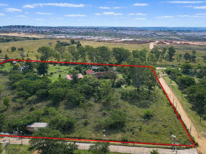 Aerial view of a large farm property with established trees, outbuildings, and perimeter fencing, situated in a semi-rural landscape.