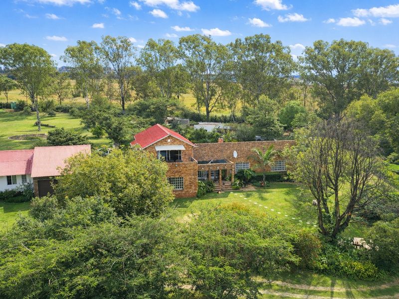 Aerial view of a brick farmhouse with a red metal roof, surrounded by extensive green lawns and mature trees on a large rural property.