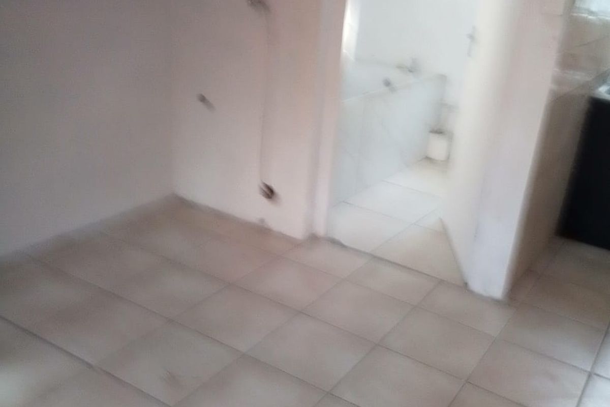 An empty hallway area with tiled flooring, showing visible wall damage and exposed wiring, leading into an adjacent bathroom space.