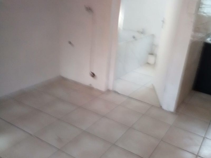 An empty hallway area with tiled flooring, showing visible wall damage and exposed wiring, leading into an adjacent bathroom space.