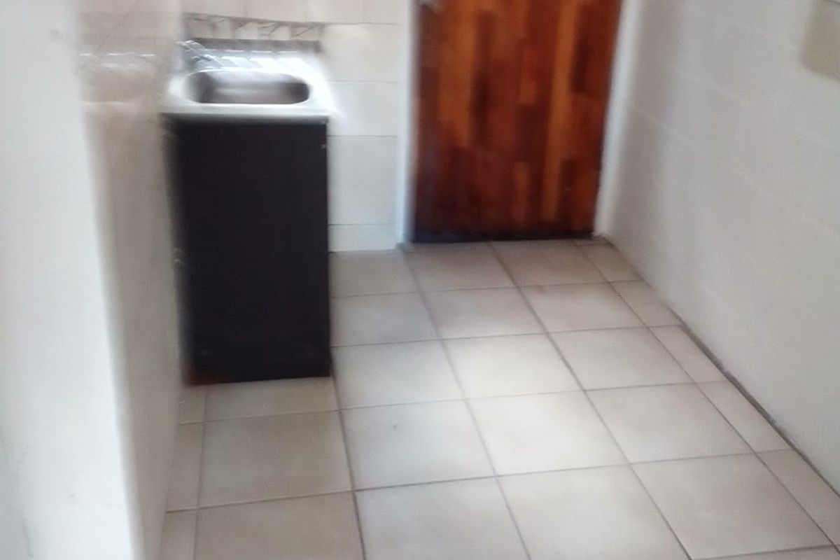 A functional laundry area featuring tiled flooring, a stainless steel sink, and a wooden door leading to the exterior.