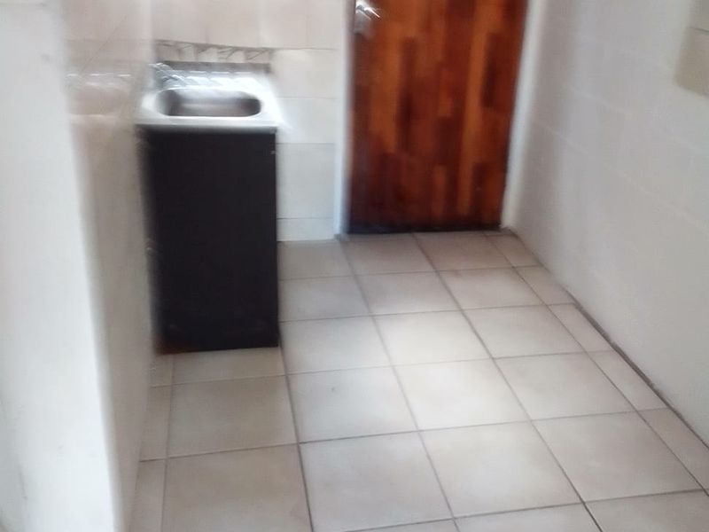 A functional laundry area featuring tiled flooring, a stainless steel sink, and a wooden door leading to the exterior.