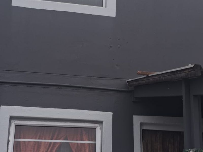 A view of the rear exterior facade featuring dark painted walls, white window frames with security bars, and a wooden door.