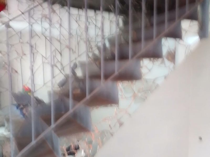 A staircase area featuring a metal balustrade and tiled flooring, currently showing significant damage to the mirrored wall paneling.