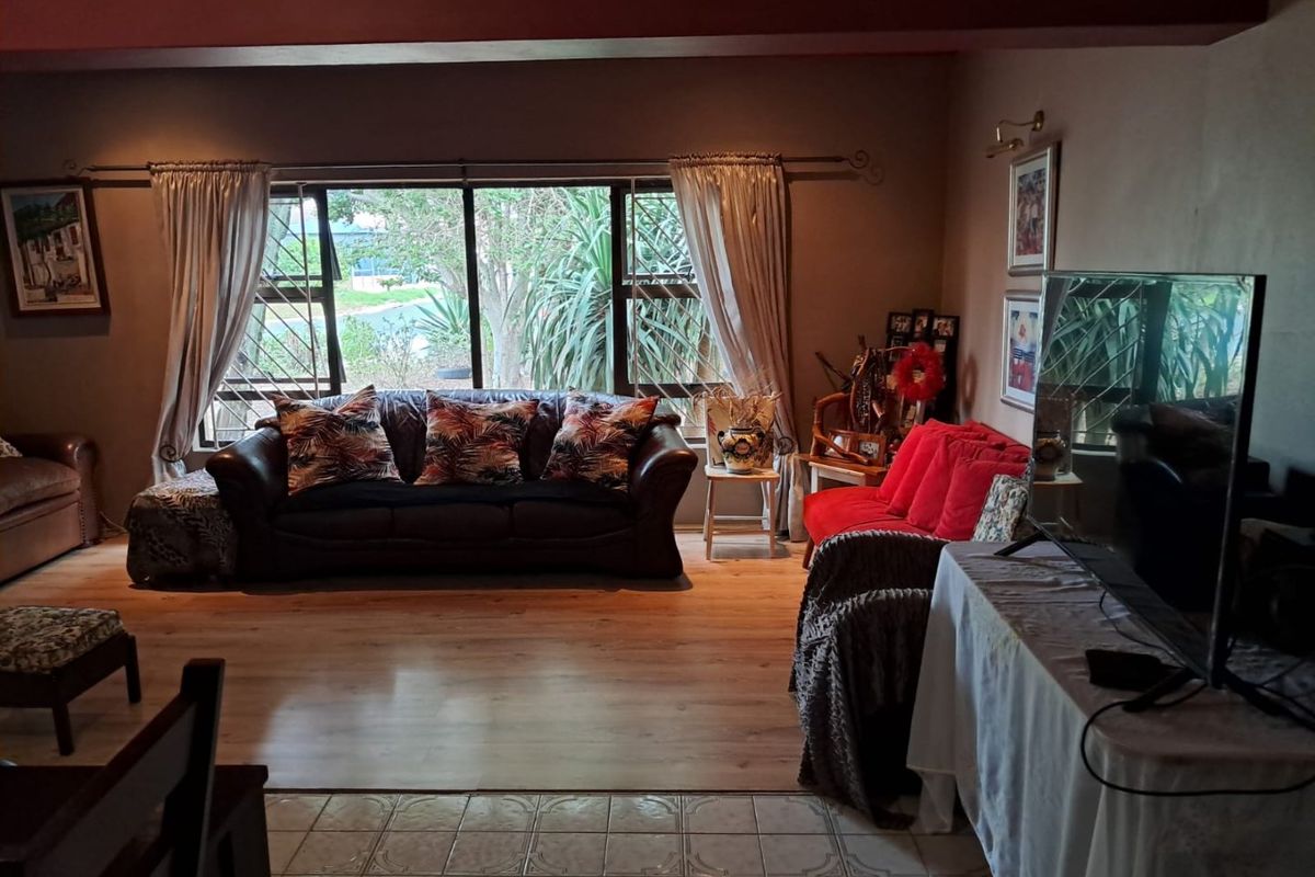 A living room featuring laminate flooring, large windows with security bars, and a transition to tiled flooring in the foreground.