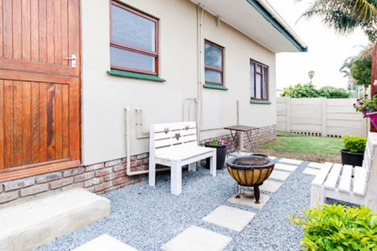 A rear exterior view featuring a gravel patio area, concrete pavers, and a timber door leading into the home, enclosed by a boundary wall.
