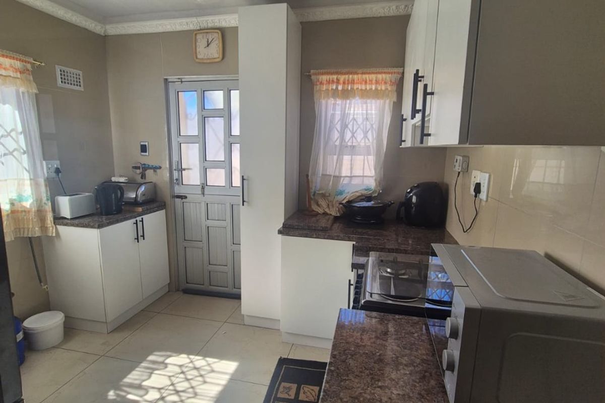 A functional kitchen featuring built-in cabinetry, laminate countertops, tiled flooring, and a secure exterior door with natural light.