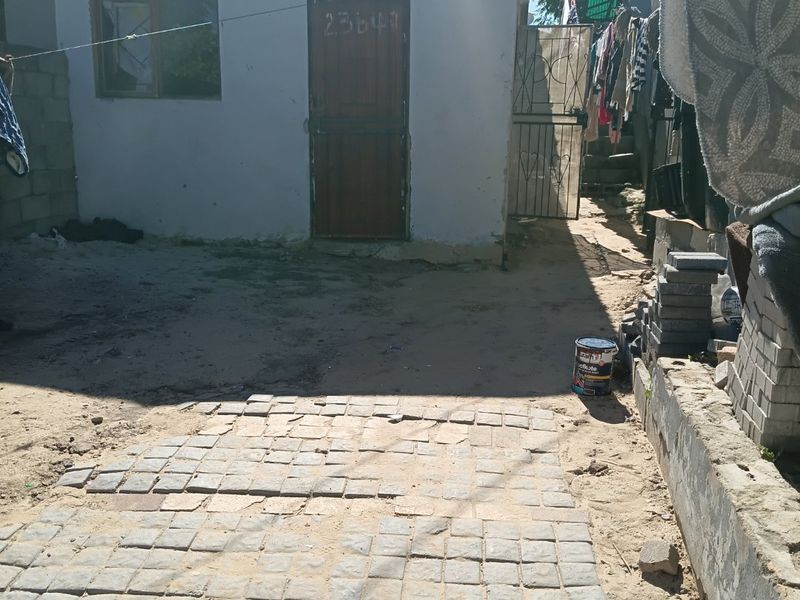 Rear exterior area featuring a paved walkway, concrete retaining wall, and access to the main structure via a metal security gate.