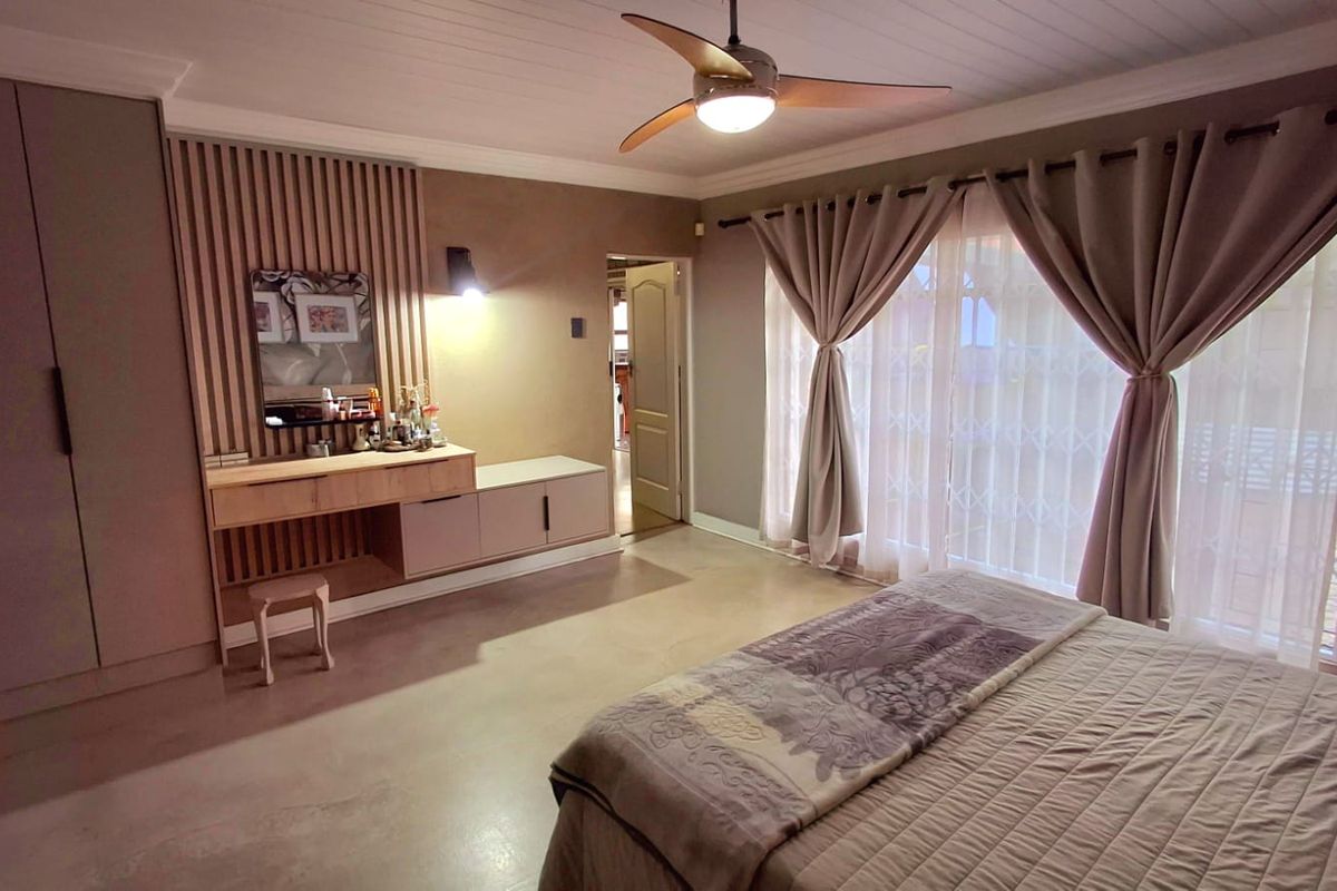 Spacious bedroom featuring polished concrete floors, built-in cupboards, a custom vanity with slatted wood detailing, and a ceiling fan.