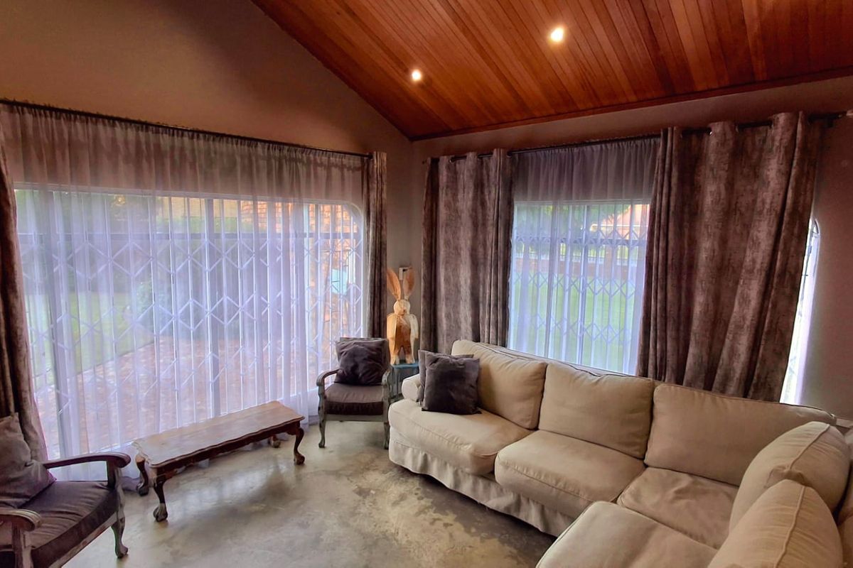 Spacious living room featuring a vaulted timber ceiling, polished concrete floors, and large sliding glass doors with security gates providing ample natural light.
