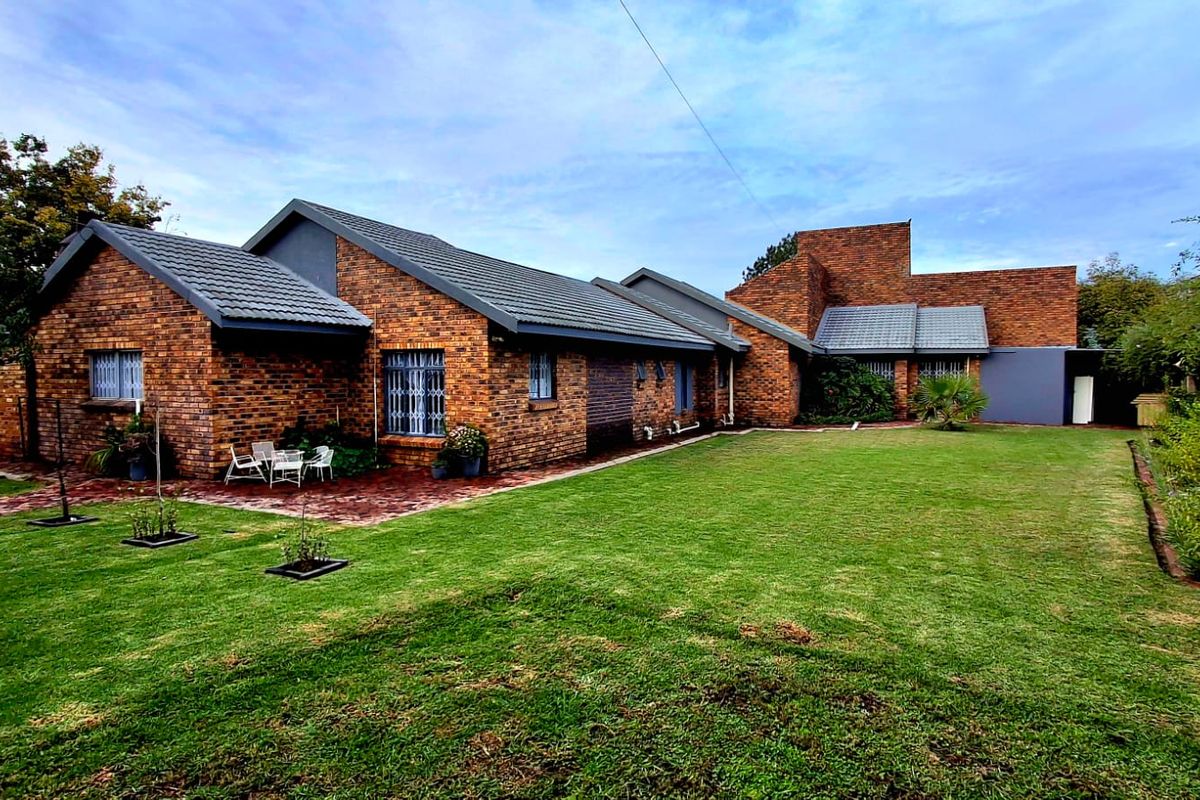 A spacious rear garden featuring a well-maintained lawn, paved patio area, and a classic face brick house exterior with tiled roofing.