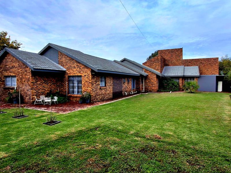 A spacious rear garden featuring a well-maintained lawn, paved patio area, and a classic face brick house exterior with tiled roofing.