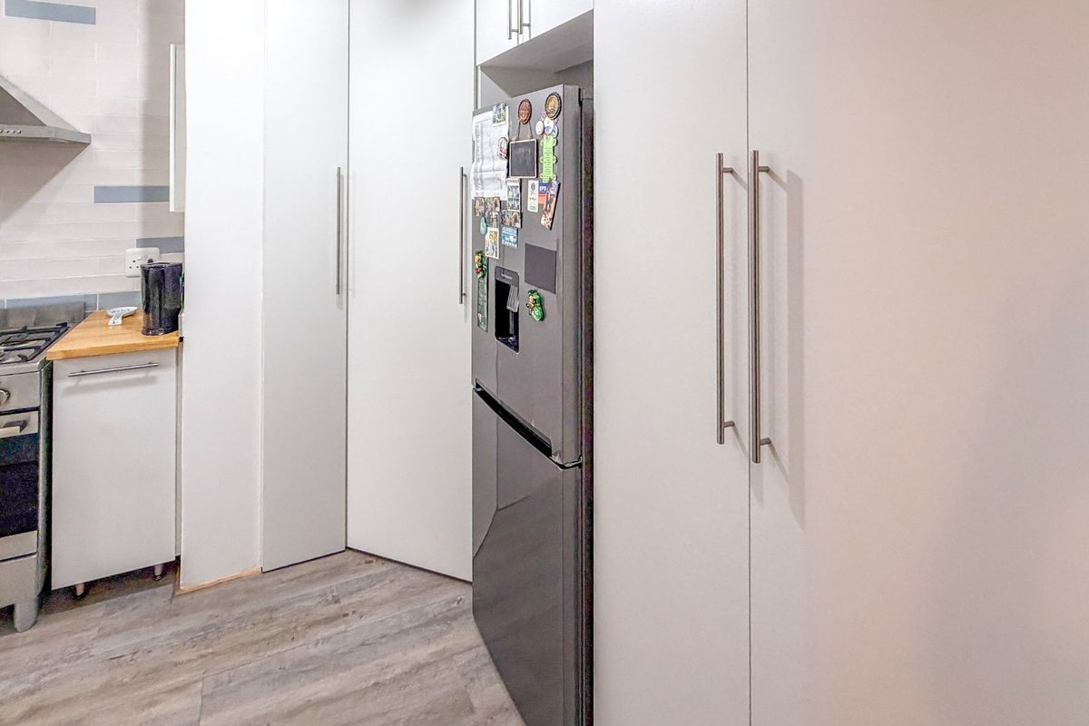 Modern kitchen featuring white cabinetry, stainless steel gas stove with extractor fan, and durable laminate flooring.