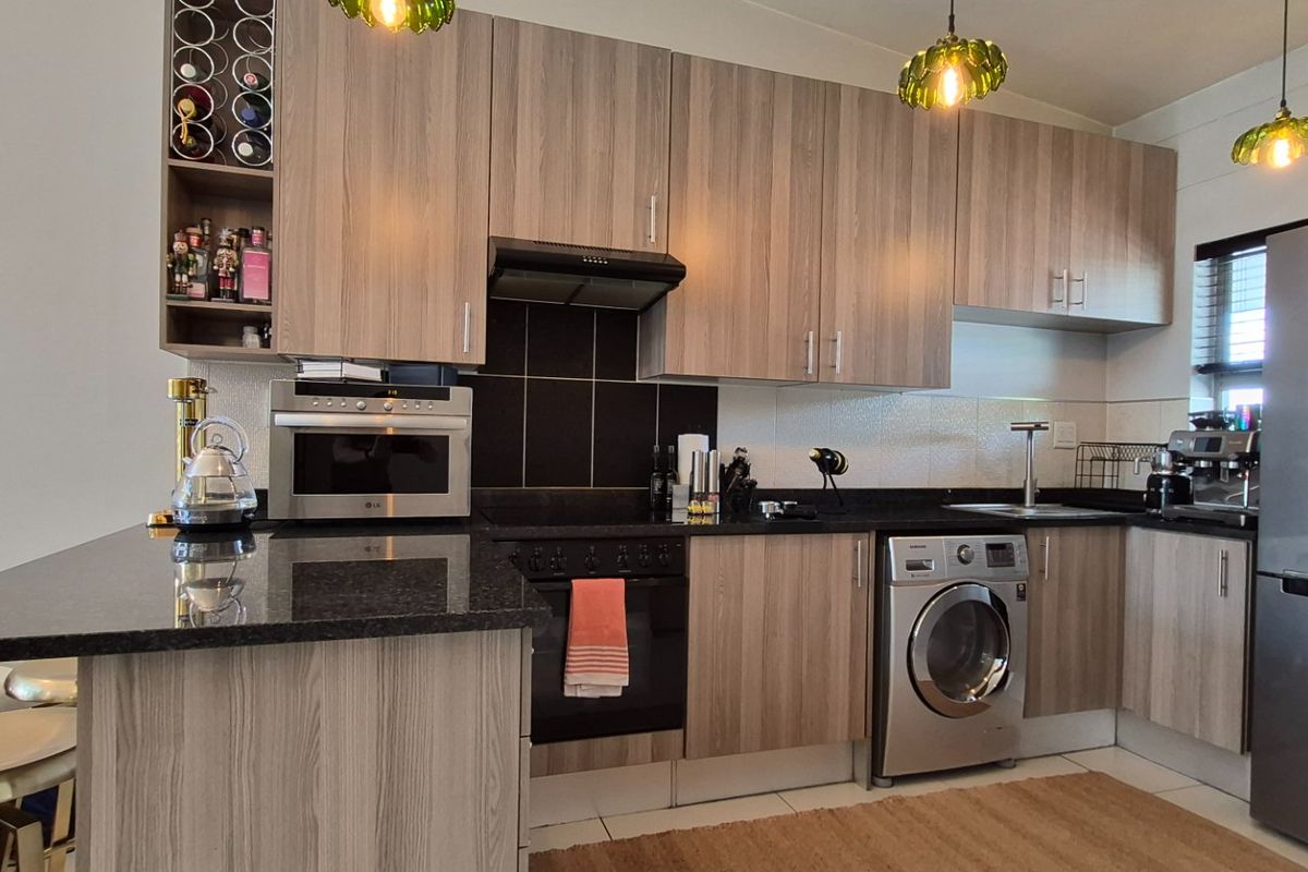 Modern kitchen featuring wood-finish cabinetry, granite countertops, a built-in oven with extractor fan, and integrated space for laundry appliances.