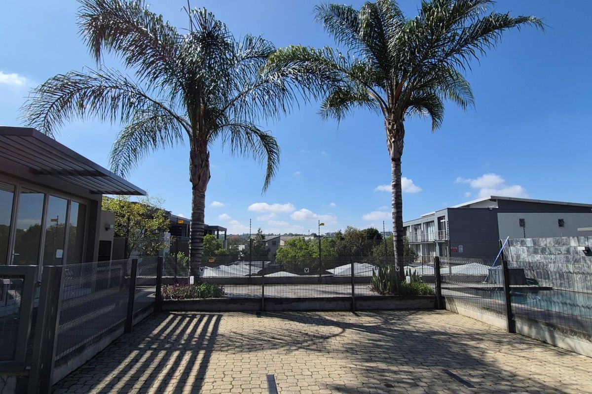 A paved outdoor area featuring wire mesh fencing, retaining walls, and mature palm trees, providing a clear view of the surrounding apartment complex.