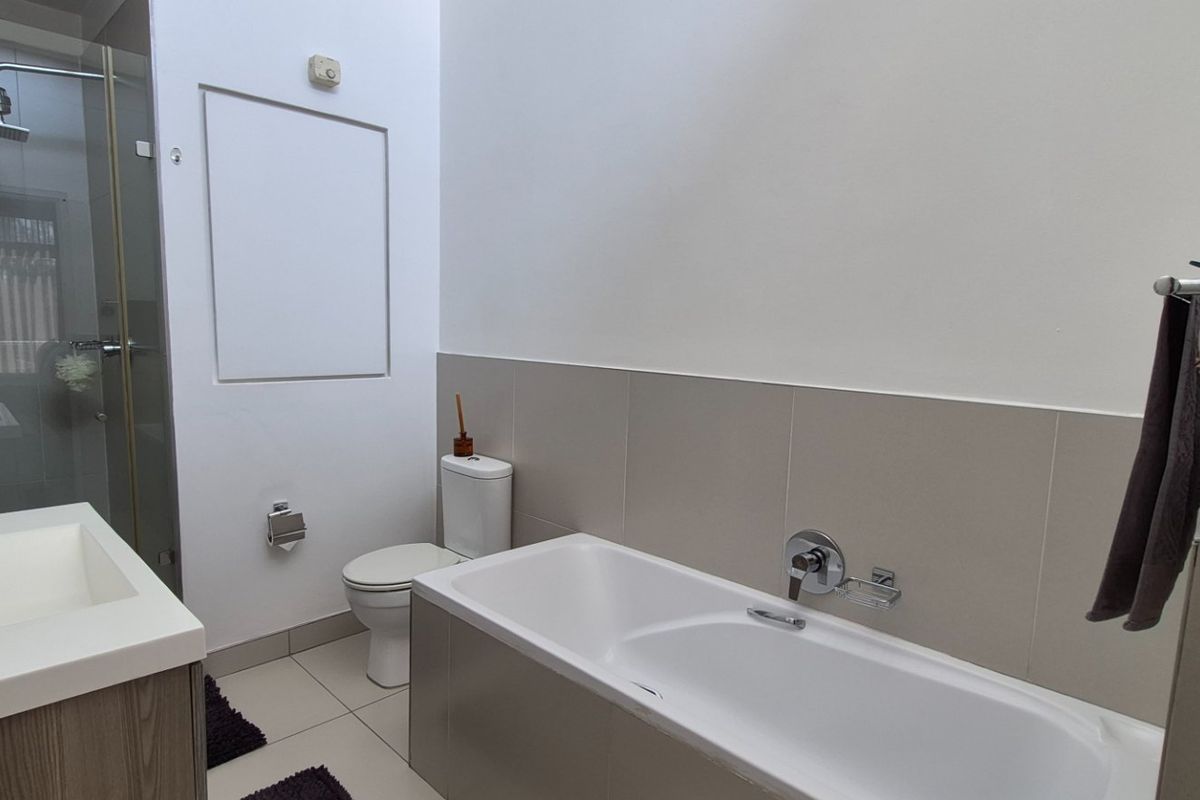 Modern bathroom featuring a glass-enclosed shower, a built-in bathtub, a vanity with basin, and neutral wall tiling.