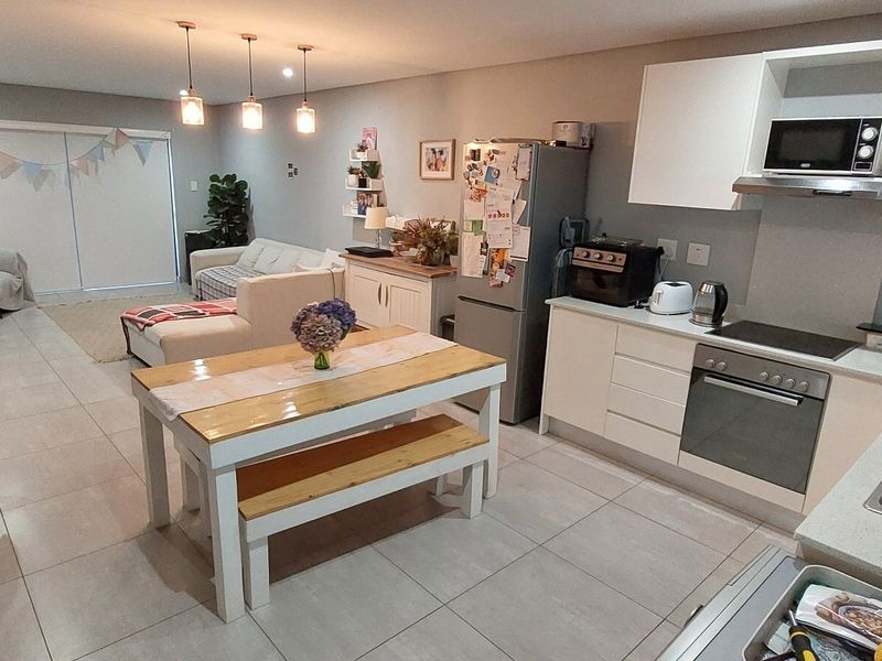 Open-plan living area featuring a modern kitchen with built-in appliances, tiled flooring, and direct access to a balcony through sliding glass doors.