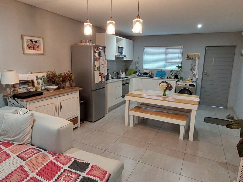An open-plan living and kitchen area featuring tiled floors, modern cabinetry, integrated appliances, and a bright, functional layout.