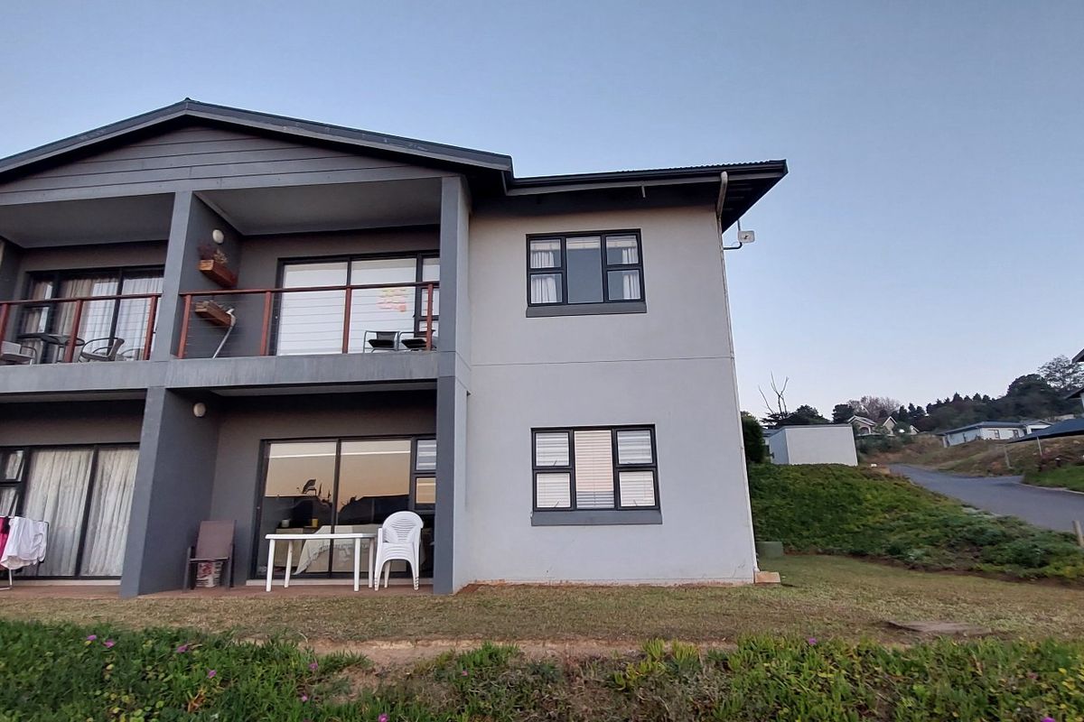 Rear elevation of a two-story apartment building featuring balconies, sliding glass doors, and aluminum window frames set in a landscaped residential complex.