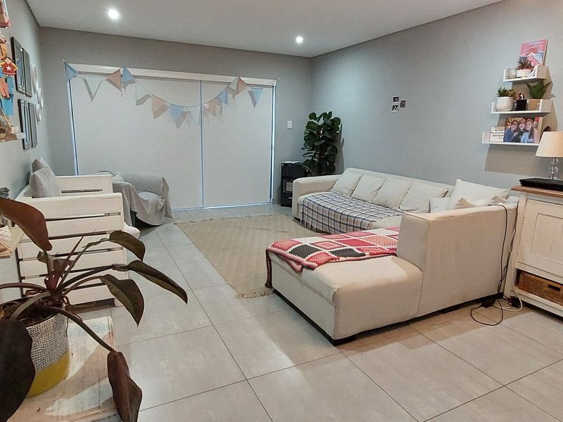 A spacious living room featuring neutral tiled flooring, recessed downlighting, and a large sliding glass door providing access to the exterior.