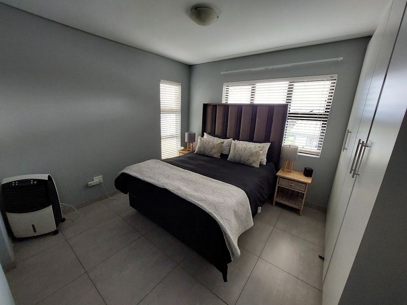 A well-maintained bedroom featuring neutral grey walls, large format floor tiles, built-in storage cupboards, and venetian blinds for privacy.