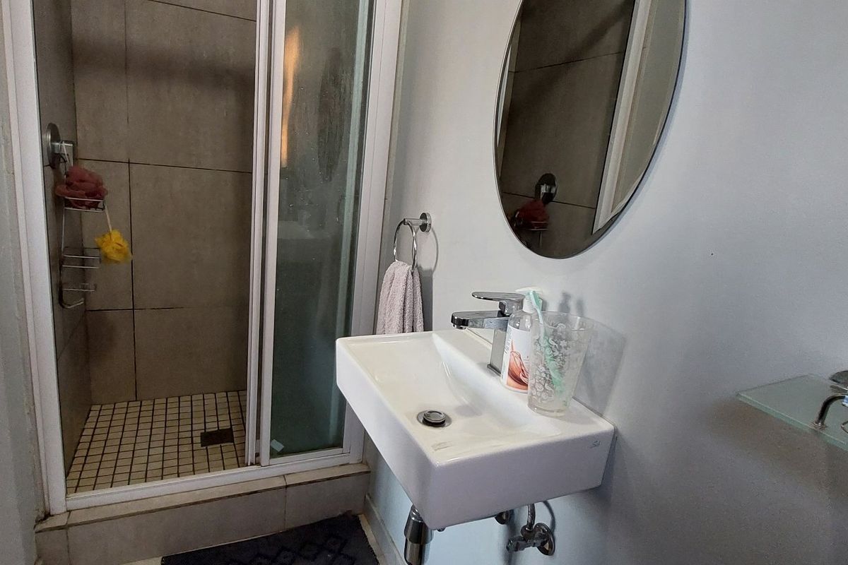 A compact bathroom featuring a wall-mounted basin with a mixer tap and a separate shower enclosure with tiled flooring.