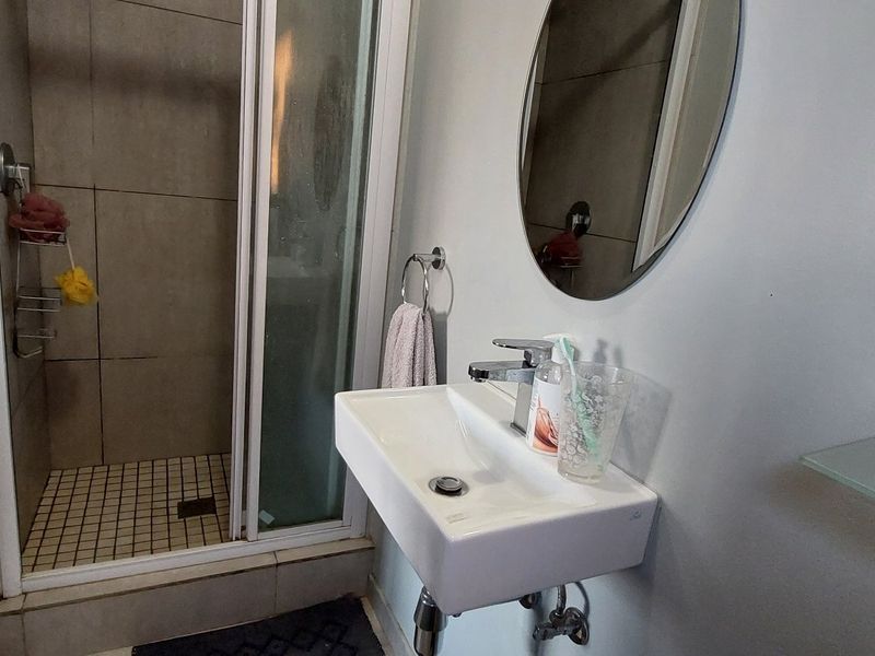 A compact bathroom featuring a wall-mounted basin with a mixer tap and a separate shower enclosure with tiled flooring.