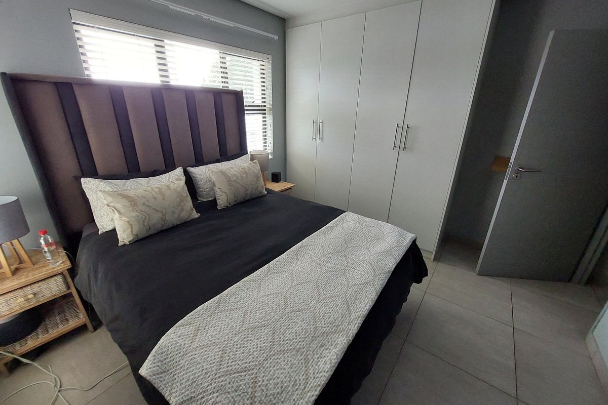A well-maintained bedroom featuring neutral tiled flooring, built-in floor-to-ceiling cupboards, and natural light through venetian blinds.