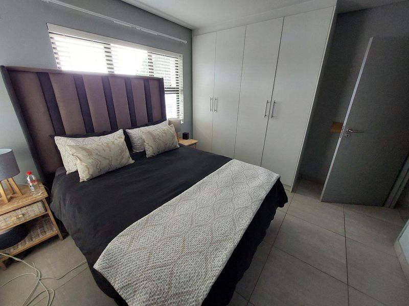 A well-maintained bedroom featuring neutral tiled flooring, built-in floor-to-ceiling cupboards, and natural light through venetian blinds.