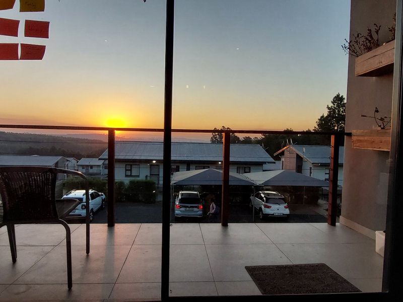 A covered balcony featuring tiled flooring, a sliding glass door, and a sunset view over the complex.