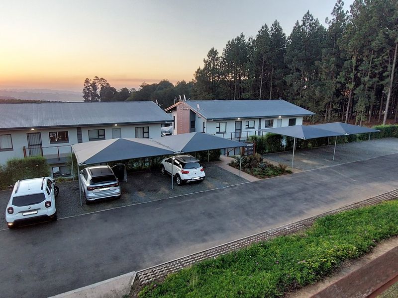 Elevated view of the apartment complex exterior featuring covered parking bays, asphalt driveway, and metal roofing at sunset.