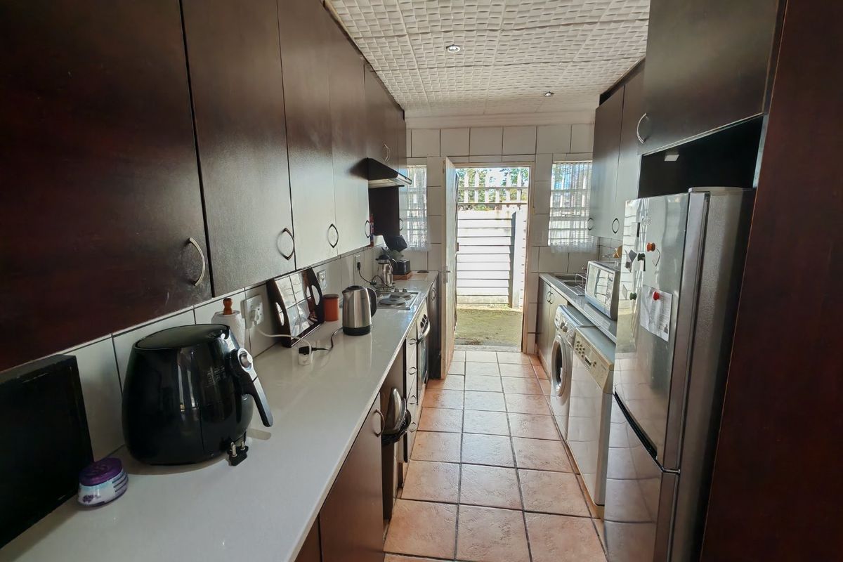 A functional galley-style kitchen featuring dark wood cabinetry, tiled flooring, and direct access to the rear exterior area.
