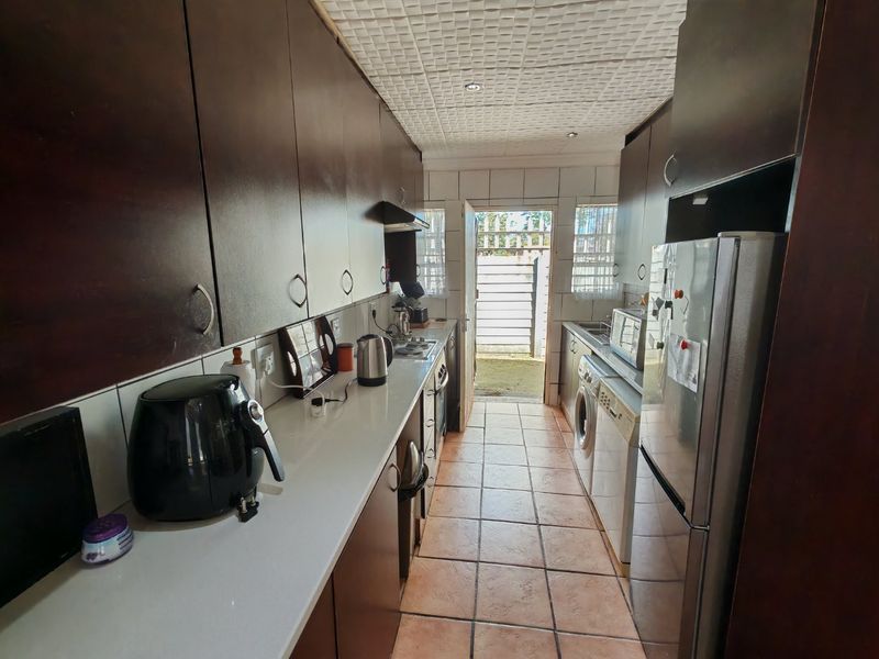 A functional galley-style kitchen featuring dark wood cabinetry, tiled flooring, and direct access to the rear exterior area.