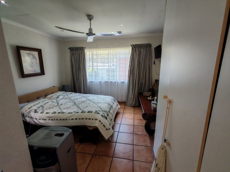 A bedroom featuring tiled flooring, a ceiling fan, and built-in storage, offering a functional space with natural light from the window.