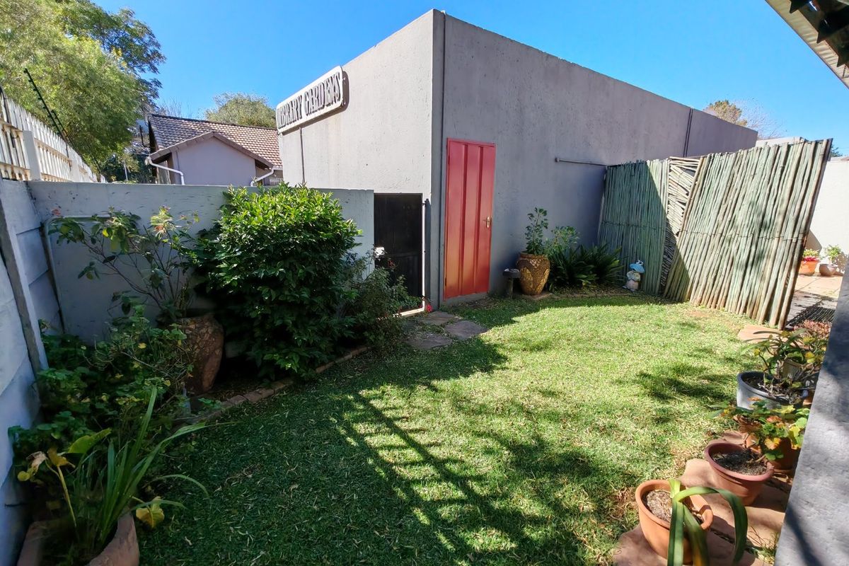 A private rear garden area featuring a lawn, boundary walls, and reed fencing, providing a compact outdoor space for the townhouse.