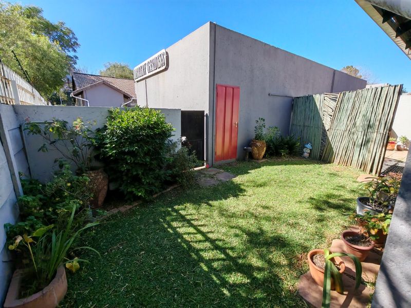 A private rear garden area featuring a lawn, boundary walls, and reed fencing, providing a compact outdoor space for the townhouse.