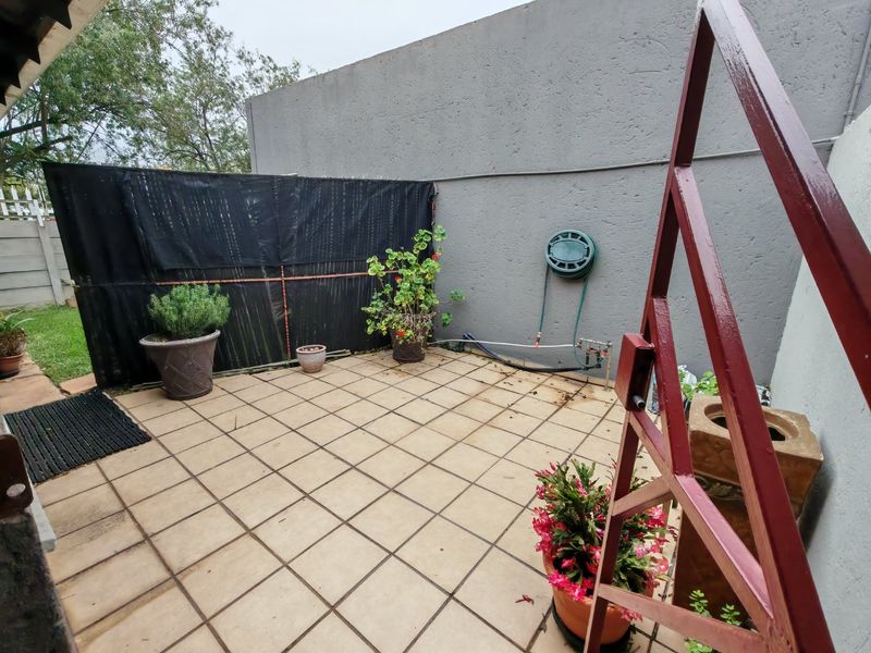 A paved outdoor patio area featuring a boundary wall, external water tap, and hose reel, providing a functional space for outdoor activities.