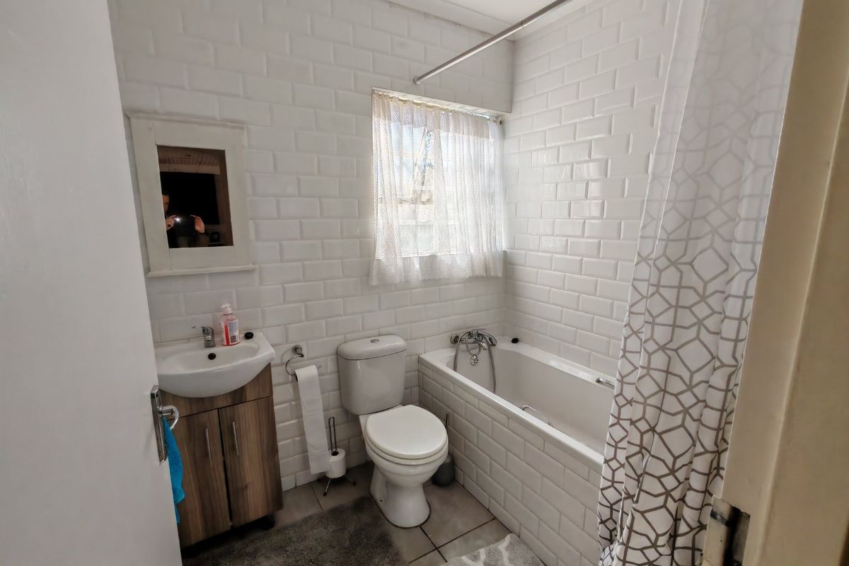A functional bathroom featuring white subway tile wall cladding, a vanity cabinet with basin, a toilet, and a bathtub with shower mixer.