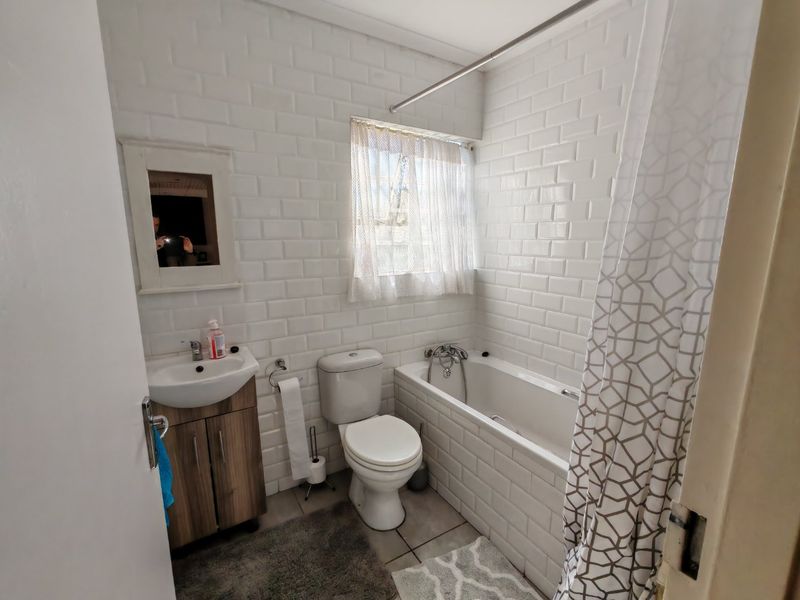 A functional bathroom featuring white subway tile wall cladding, a vanity cabinet with basin, a toilet, and a bathtub with shower mixer.