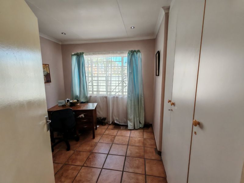 A functional bedroom featuring tiled flooring, built-in cupboards for storage, and recessed downlighting, with security bars installed on the window.