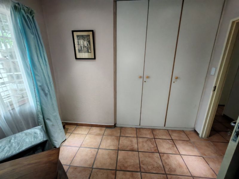 A bedroom featuring tiled flooring and built-in cupboards, offering a functional space with potential for modern updates.