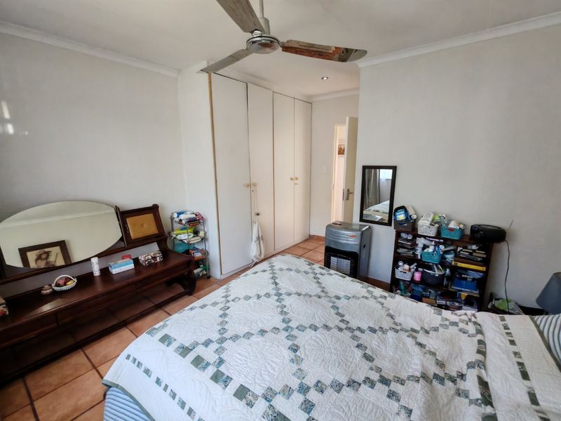 A bedroom featuring built-in cupboards, a ceiling fan, and tiled flooring, offering a functional space with potential for modernization.