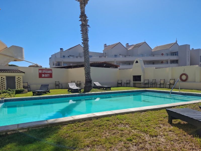 Communal swimming pool area featuring a built-in braai, perimeter wall, and landscaped lawn space within the apartment complex.