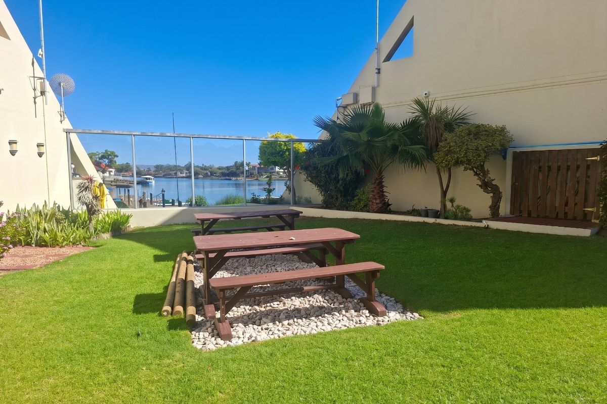 A well-maintained rear garden area featuring a manicured lawn, pebble landscaping, and a glass balustrade overlooking the water.