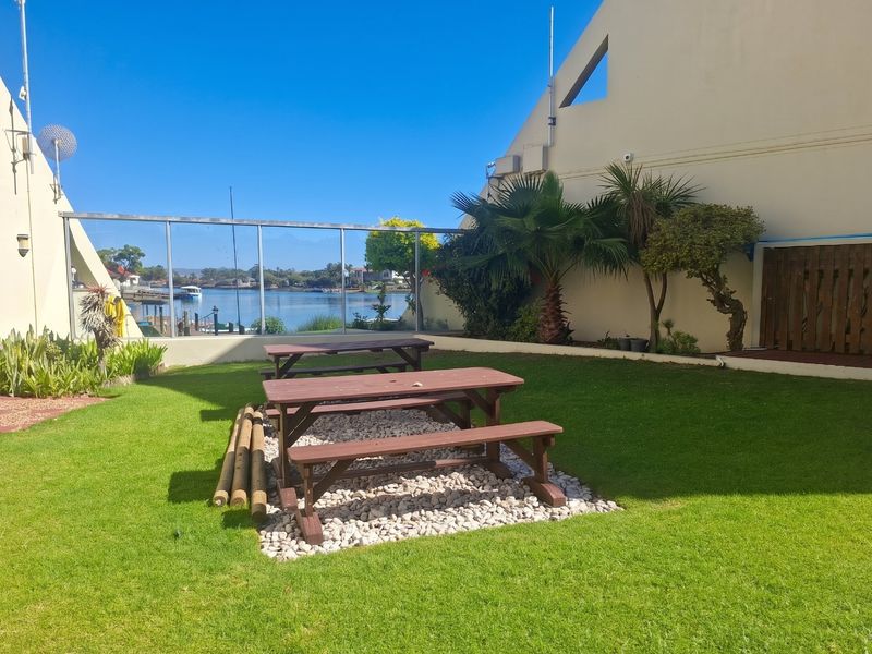 A well-maintained rear garden area featuring a manicured lawn, pebble landscaping, and a glass balustrade overlooking the water.