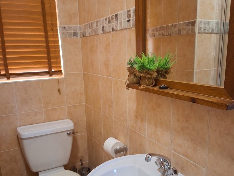 A functional bathroom featuring neutral ceramic wall tiles, a pedestal basin with chrome mixer, and a wooden framed mirror.