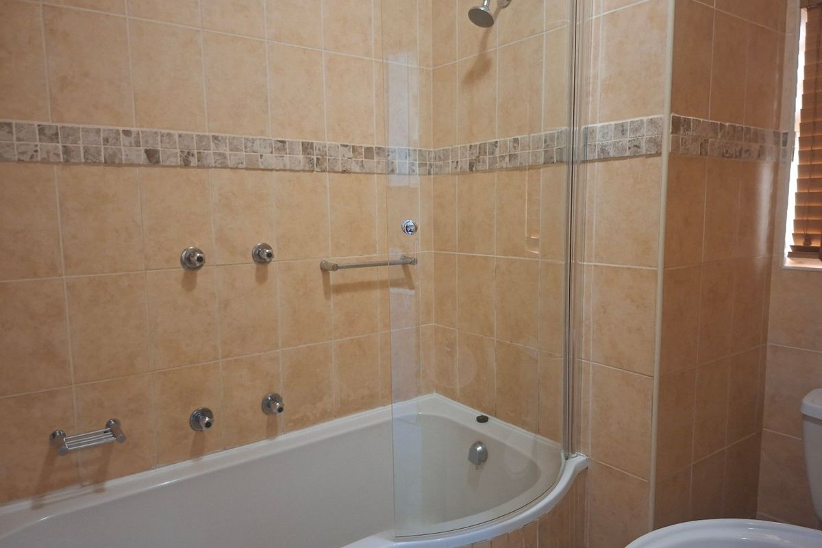 A functional bathroom featuring a bathtub with a glass shower screen, tiled walls with decorative accents, and standard sanitary fixtures.