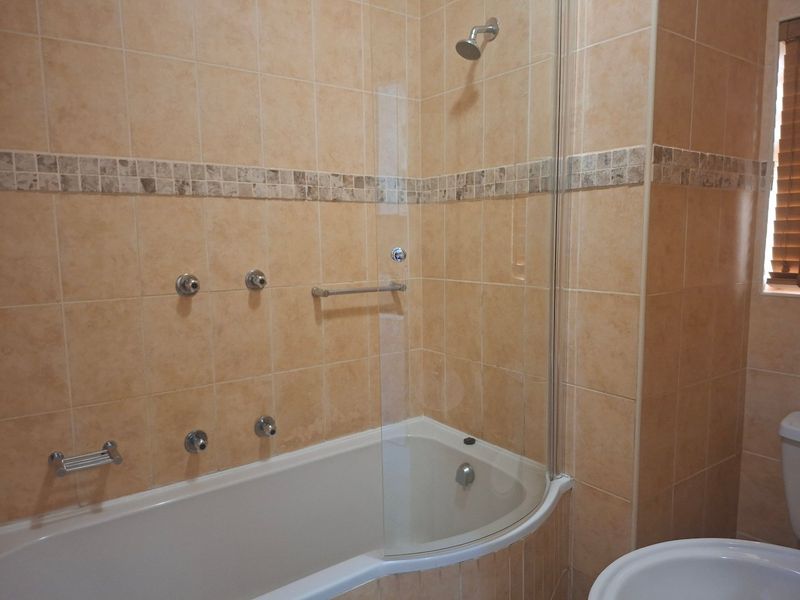 A functional bathroom featuring a bathtub with a glass shower screen, tiled walls with decorative accents, and standard sanitary fixtures.
