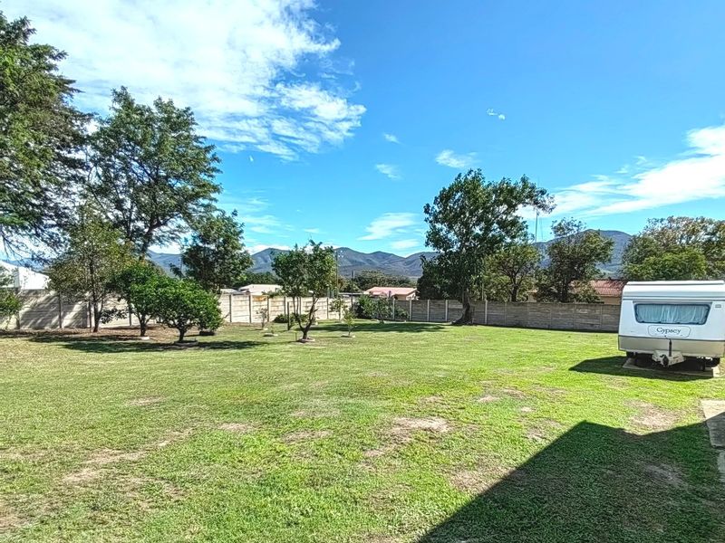 A spacious, well-maintained garden featuring a large lawn area and secure precast concrete boundary walls with mountain views in the background.