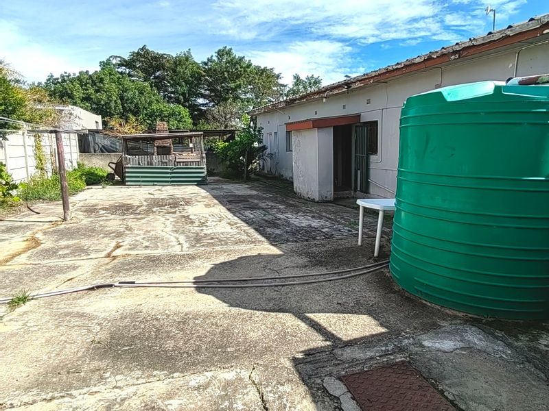 Rear exterior area featuring concrete paving, a built-in braai, and a large water storage tank against the house wall.
